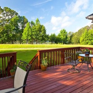 Giardino con decking in legno di sucupira, che ospira arredi da giardino e, attraverso una scala, dà su un grande prato verde delimitato, in fondo, da molti alberi