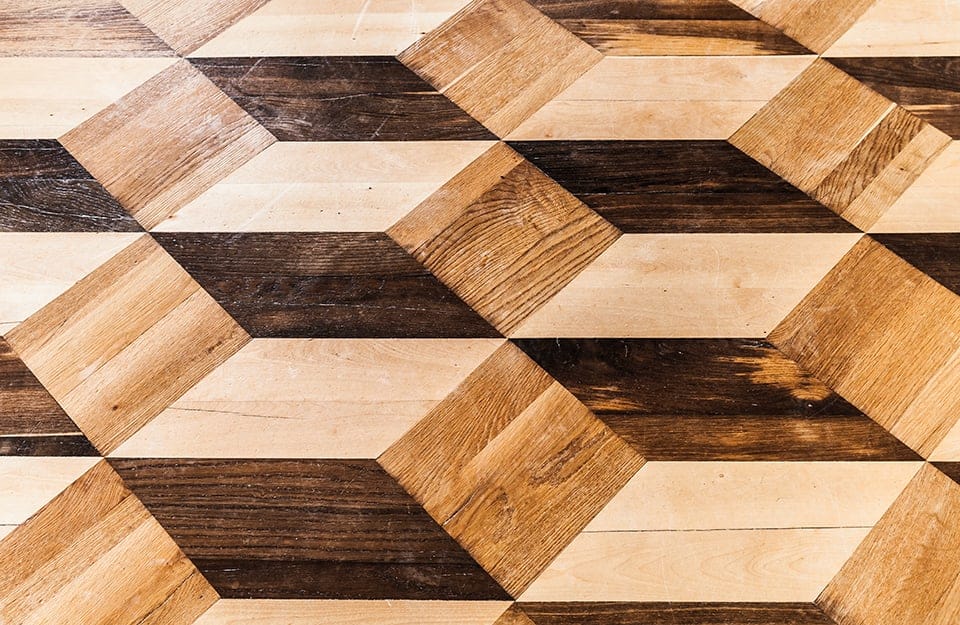Dettaglio di un pavimento a parquet intarsiato con motivi a rombi in tre diverse essenze, che danno l'idea di cubi
