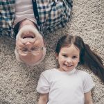Un nonno e una nipotina sorridenti e sdraiati su una moquette chiara