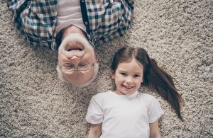 Un nonno e una nipotina sorridenti e sdraiati su una moquette chiara