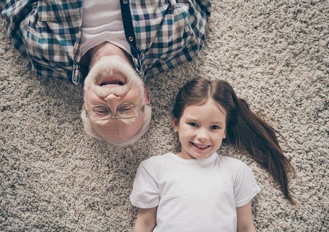 Un nonno e una nipotina sorridenti e sdraiati su una moquette chiara