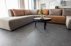 Un luminoso salotto con un grande divano ad angolo, tavolino da caffè e pavimento in linoleum grigio
