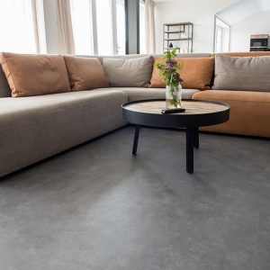 Un luminoso salotto con un grande divano ad angolo, tavolino da caffè e pavimento in linoleum grigio