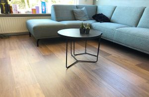 Un salotto con grande divano ad angolo, tavolino da caffè e pavimento in linoleum effetto-parquet