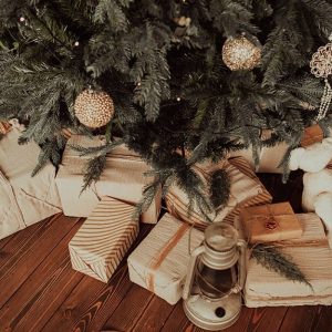 Dettaglio di un albero di Natale con dei pacchetti incartati con carta bianca sistemati sotto ai rami e sopra al parquet