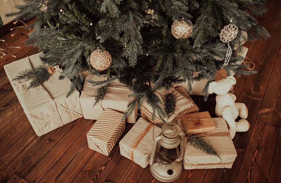 Dettaglio di un albero di Natale con dei pacchetti incartati con carta bianca sistemati sotto ai rami e sopra al parquet