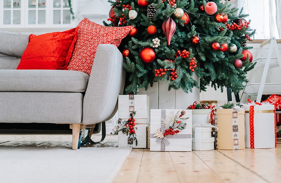 Dettaglio di un salotto con parquet, divano grigio, tappeto grigio, albero di Natale e pacchi regalo