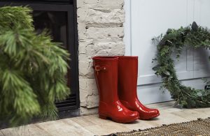 Degli stivali rossi lasciati su un pavimento in parquet, accanto a una ghirlanda natalizia e a un camino