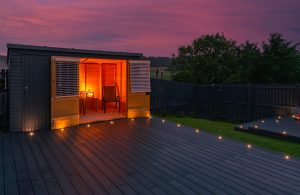 Vista al tramonto di un piccolo bungalow con decking esterno. Le luci interne sono accese