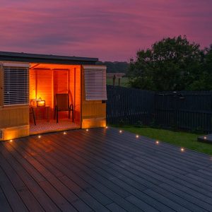 Vista al tramonto di un piccolo bungalow con decking esterno. Le luci interne sono accese