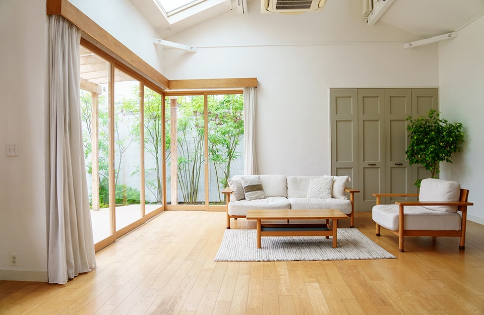 Grande e luminoso salotto con parete finestrata che dà su un giardino, arredamente in stile scandinavo, lucernario e parquet dorato