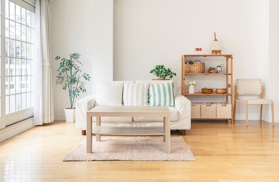 Luminoso salotto in stile nordico, con sofà bianco, grande finestra, tavolino da caffè, scaffale in legno naturale e parquet di colore giallo-dorato