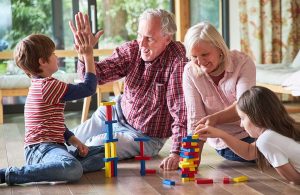 Nonno e nonna giocano con nipotino e nipotina con le costruzioni di legno sul parquet