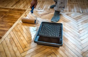 In uomo di cui si vede una mano e i piedi (con calzini) sta passando con un rullo dell'olio su un parquet