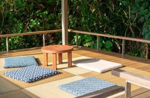 Area di un decking da esterno immerso nel verde, con stuoie, cuscini e sgabelli