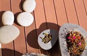 Dettaglio di un decking in legno da esterno visto dall'alto con piantine in vasi di forme tondeggianti irregolari e grandi ciottoli