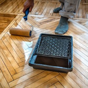 In uomo di cui si vede una mano e i piedi (con calzini) sta passando con un rullo dell'olio su un parquet