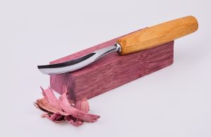 Una sgorbia appoggiata su un blocco di legno di amaranto, con alcuni trucioli accanto