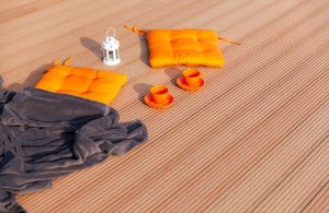 Dettaglio di un'area esterna con decking in legno di robinia, con cuscini e tazze arancioni, un accappatoio scuro e una lanterna