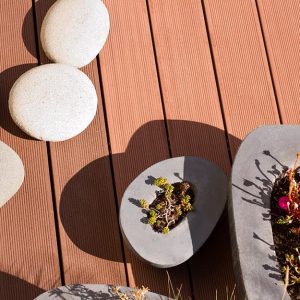 Dettaglio di un decking in legno da esterno visto dall'alto con piantine in vasi di forme tondeggianti irregolari e grandi ciottoli