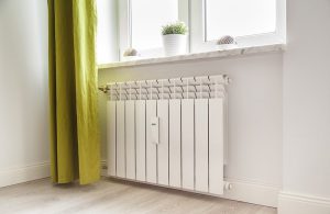 L'angolo luminoso di una stanza con pavimento a parquet, radiatore bianco, tenda verde acido e piantine sul davanzale della finestra