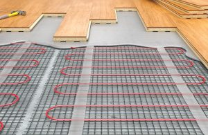 Un impianto di riscaldamento radiante a pavimento, mostrato in sezione, con tubi riscaldati, copertura e parquet