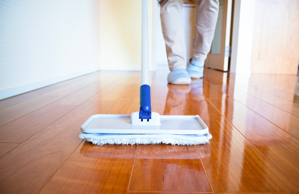 Prospettiva ad altezza pavimento di una persona in pantofole sta passando un mocio su un parquet lucido