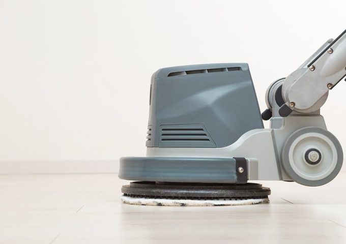 Primo piano su una lucidatrice professionale che sta passando la cera su un parquet bianco