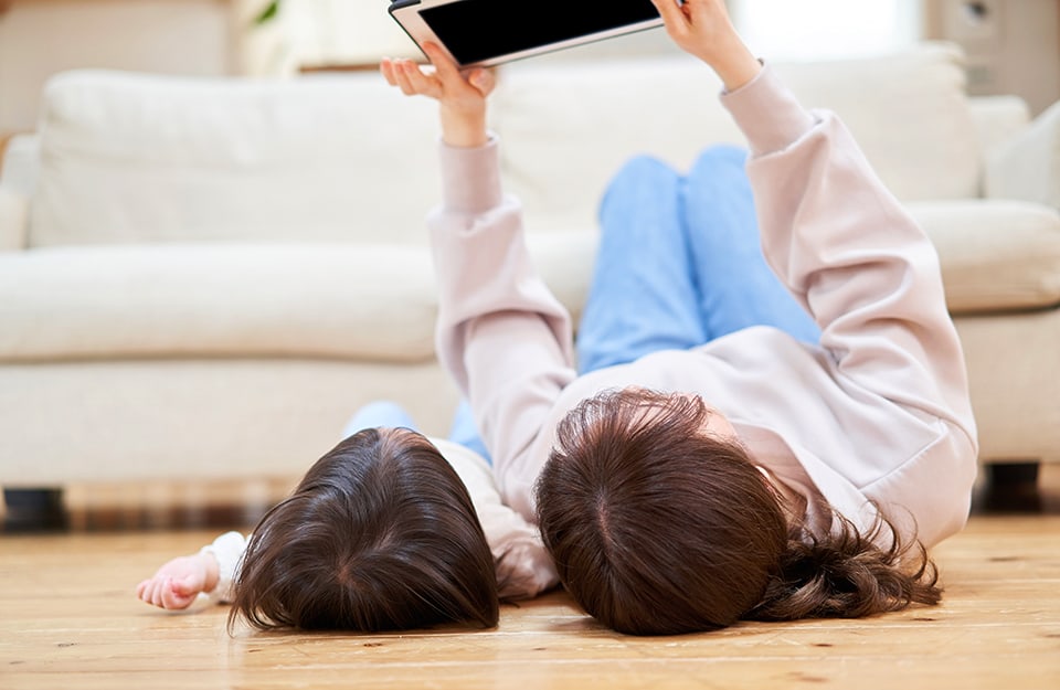 Una mamma e una figlia sdraiate sul parquet del salotto mentre guardano lo schermo di un tablet