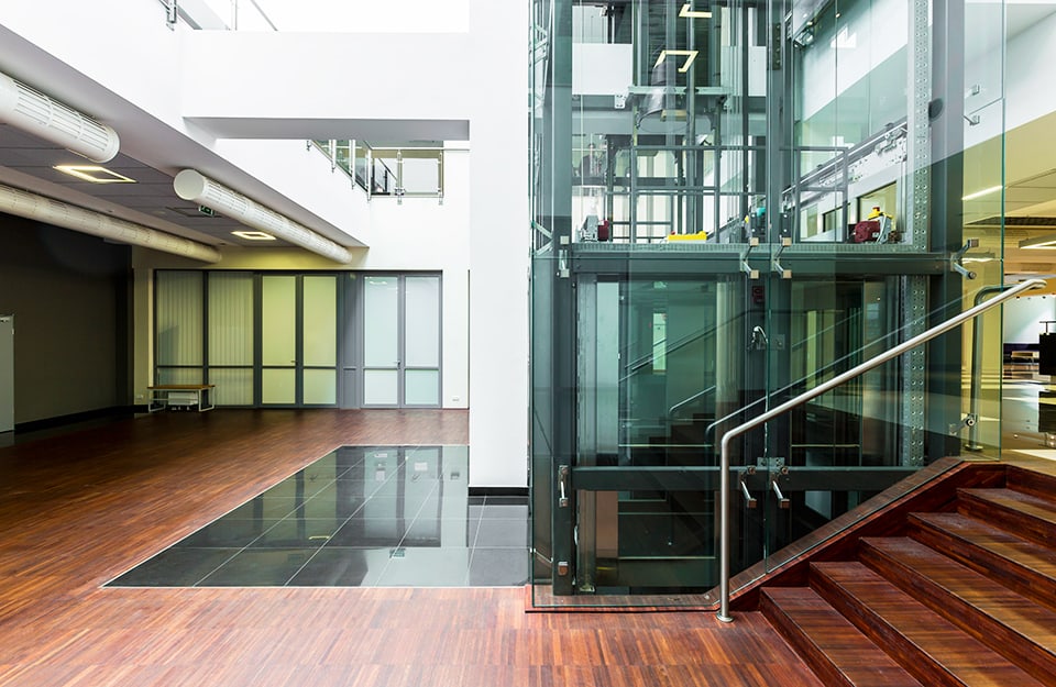 Grande atrio di edificio pubblico o albergo, con ascensore trasparente, scale e parquet industriale