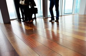 Dettaglio sul pavimento in parquet di un ufficio open space con molte finestre e persone di cui non si vedono i volti riunite a parlare
