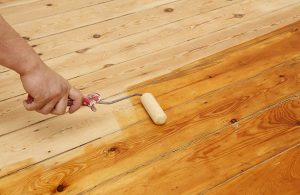 Mano di un uomo che con un rullo sta applicando dell'olio a un parquet
