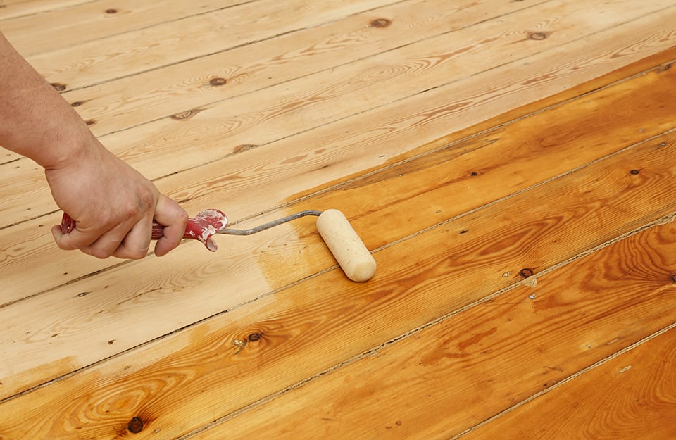 Mano di un uomo che con un rullo sta applicando dell'olio a un parquet
