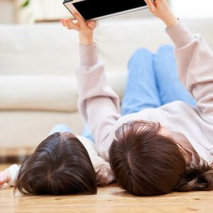 Una mamma e una figlia sdraiate sul parquet del salotto mentre guardano lo schermo di un tablet