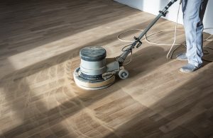 Un uomo sta passando una macchina levigatrice sul parquet in una stanza altrimenti vuota