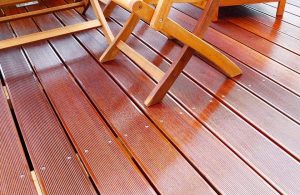 Dettaglio di un decking esterno in legno di bangkirai. Si intravedono anche le gambe un tavolo e sedie da giardino