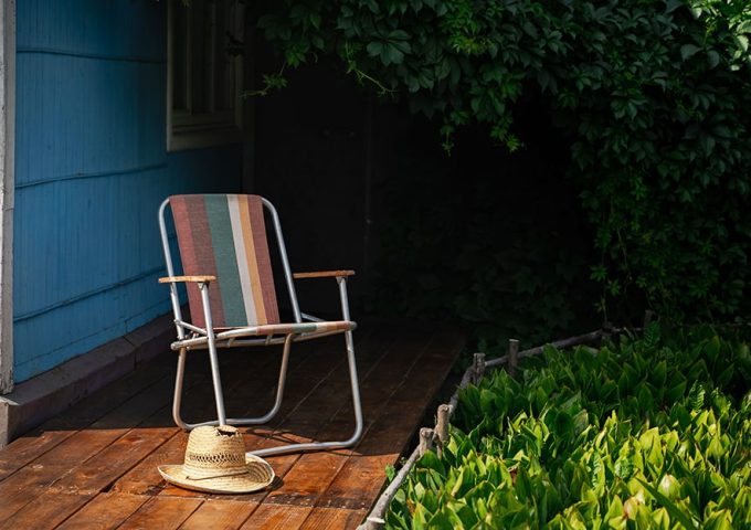 Giardino con vialetto in decking e sedia pieghevole da esterno colorata con accanto un cappello