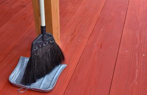 Dettaglio su un parquet da esterno con scopa e paletta in metallo poggiate a una colonna in legno