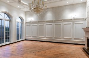 Stanza vuota di un palazzo antico, con boiserie bianche alle pareti, grande lampadario a candelabro di cristallo, finestre ad arco e pavimento in parquet