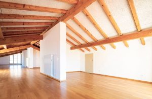 Grande ambiente open space con divisori e porti in una casa ristrutturata con travi a vista, muri bianchi e pavimento in parquet