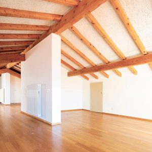 Grande ambiente open space con divisori e porti in una casa ristrutturata con travi a vista, muri bianchi e pavimento in parquet