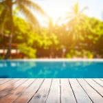 Vista dal basso di una piscina immersa nel verde, con in primo piano le assi di legno del decking a bordo piscina