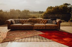 Sofà in pelle su una terrazza con ringhiera in metallo affacciata sulla campagna. Sotto al divano ci sono due tappeti orientali che coprono parzialmente il decking
