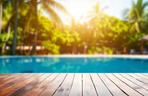 Vista dal basso di una piscina immersa nel verde, con in primo piano le assi di legno del decking a bordo piscina