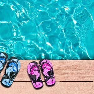 Vista dall'alto di due paia di infradito di colori diversi (azzurre e magenta) lasciate sulle assi in legno del decking a bordo piscina