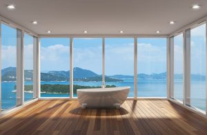 Stanza completamente finestrata con soffitto bianco e faretti, affacciata su un panorama costiero. Nella stanza, con pavimento in parquet, si trova soltanto una vasca da bagno bianca dalle linee moderne e tondeggianti