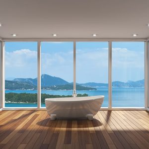 Stanza completamente finestrata con soffitto bianco e faretti, affacciata su un panorama costiero. Nella stanza, con pavimento in parquet, si trova soltanto una vasca da bagno bianca dalle linee moderne e tondeggianti