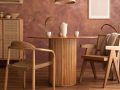 Stanza con parete marrone-rossiccia con effetto limewash, tavolo in legno circolare, sedie in legno in stile scandinavo, armadietto con ante in vimini, pavimento in parquet