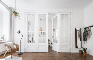 Spazioso ingresso di una casa sui toni del bianco, con porta a vetri e parquet scuro che prosegue nell'altra stanza