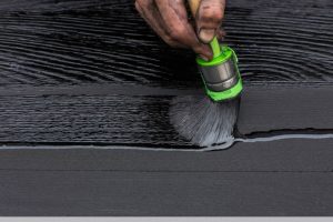 Una mano d'uomo sporca di nero impugna un pennello col quale sta trattando con olio impregnante una tavola di legno bruciato con la tecnica dello Yakisugi